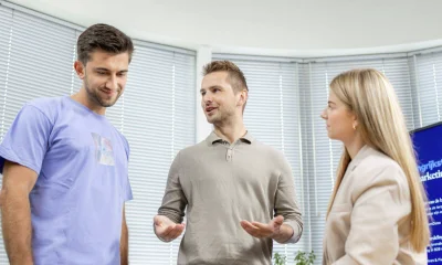 Een afbeelding van twee mannen en een vrouw in gesprek op een tafel.