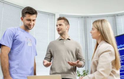 Een afbeelding van twee mannen en een vrouw in gesprek op een tafel.